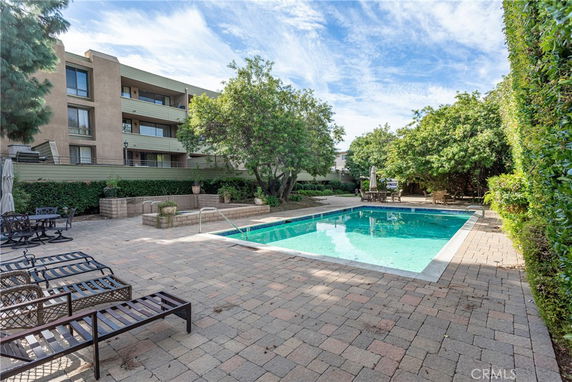 Outdoor swimming pool area with lounge chairs and surrounding trees near a residential building.
