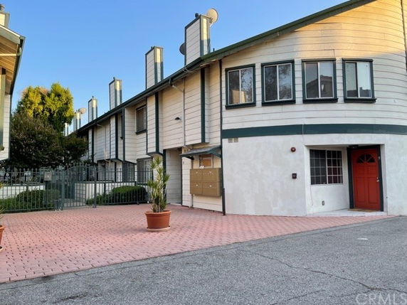 Front view of a multi-story building with multiple chimneys and a paved area in front.