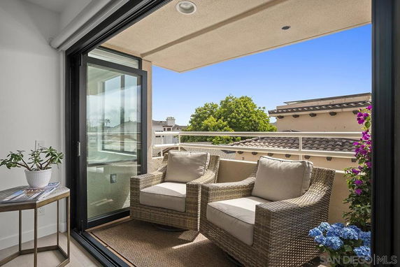 Small balcony with wicker chairs overlooking neighboring buildings.
