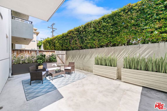 Outdoor patio area with seating and planters against a green hedge.