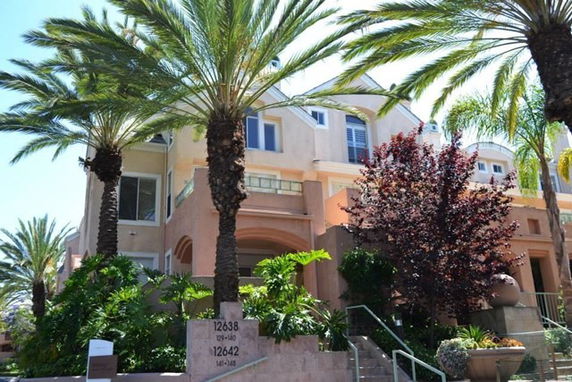 Front view of a multi-story house with palm trees and a staircase leading to the entrance.