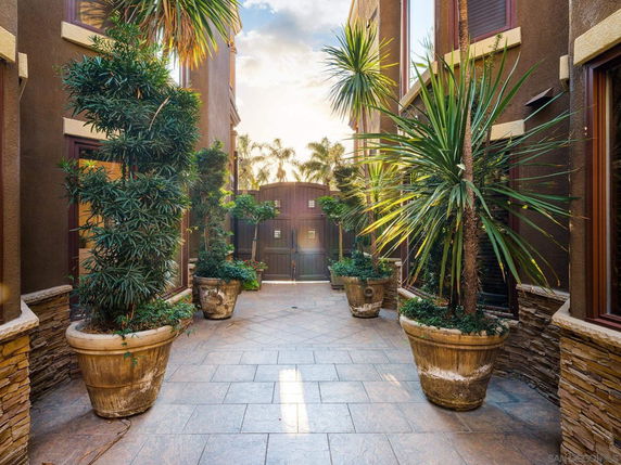 Courtyard view between buildings with potted plants and a gated entrance.