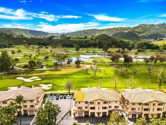 Aerial view of apartment buildings with a golf course and hilly landscape in the background.
