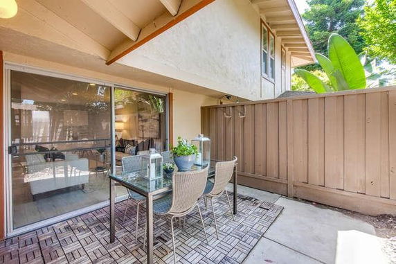 Patio area with a glass table and chairs next to a house with sliding glass doors.