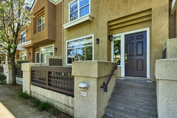 Front view of a townhouse with a brown door and windows, featuring a small staircase and fence.