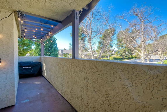 Outdoor view from a balcony with decorative lights and a covered grill overlooking trees and neighboring buildings.