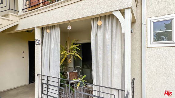 Balcony area of a residential building with hanging plants and light curtains.