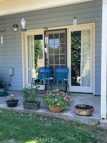 Partial front view of a house with a small porch featuring two chairs and potted plants.