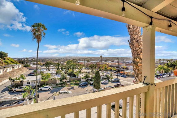 Panoramic view from a balcony overlooking a neighborhood with streets, cars, and palm trees.