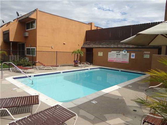 Outdoor swimming pool next to a building with lounge chairs and umbrellas.