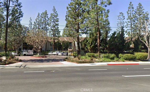 Front view of a residential building with multiple trees and a parking area in front.