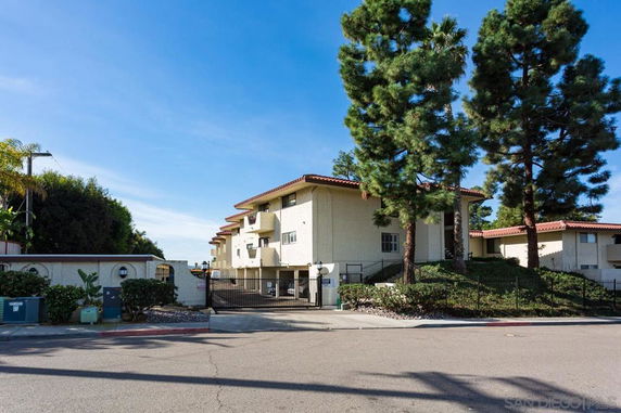 Front view of a multi-story building with a gated entrance and surrounding trees.