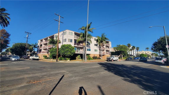 Front view of a multi-story apartment building on a street corner with palm trees.