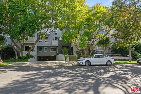 Front view of a modern multi-story building with large windows and trees lining the street.