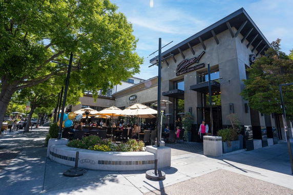Front view of a modern commercial building with patio seating and large umbrellas.