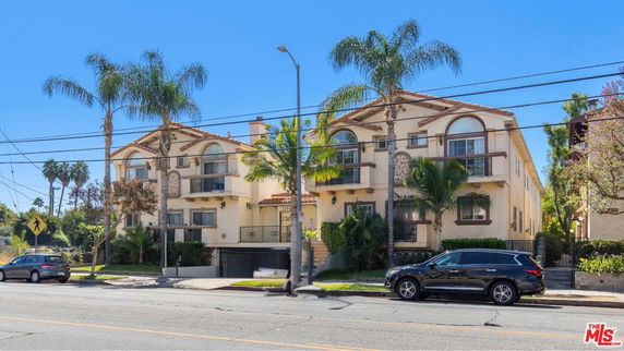 Front view of a multi-story residential building with arch windows and palm trees.