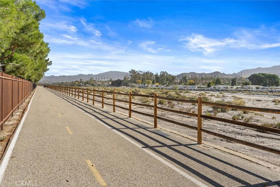 Pathway alongside a rail fence with trees and distant mountains.