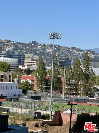 Wide view of an outdoor sports field with people, surrounded by trees and buildings.