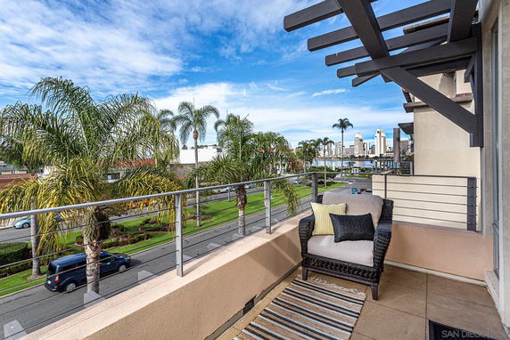 Balcony view with outdoor seating overlooking a street lined with palm trees and distant skyline.