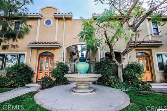 Front view of a two-story house with arched and circular windows, featuring a central fountain and decorative entryways.