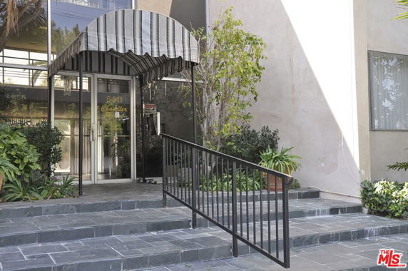 Front entrance view of a building with a striped awning and black railing.