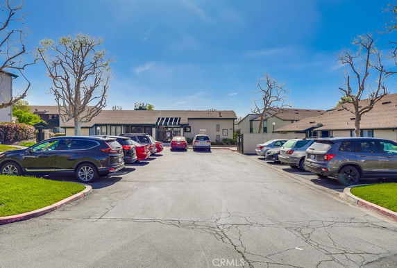 Outdoor parking area with several parked cars in front of residential buildings.