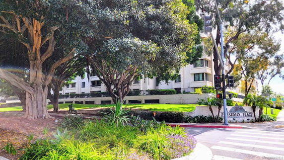 Front view of a multi-story residential building with balconies surrounded by trees and greenery.