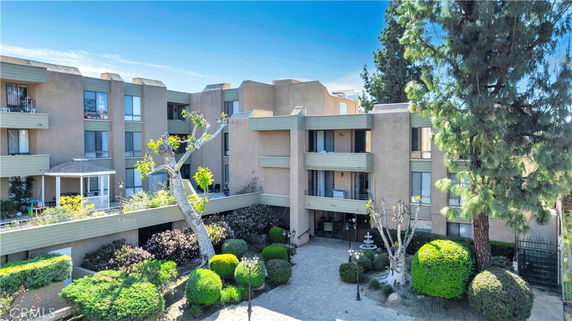 Front view of a multi-story residential building with a courtyard area and trees.