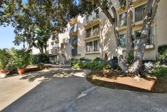 Front view of a multi-story residential building with balconies and surrounded by trees.