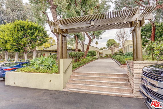 Front view of a building with a pergola, steps leading up to the entrance, and surrounding greenery.