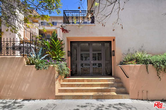Front view of a multi-story building entrance with steps and decorative plants.