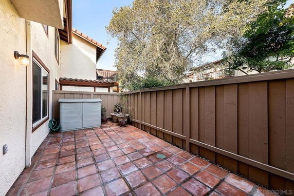 Outdoor tiled area with wooden fence and small storage shed.