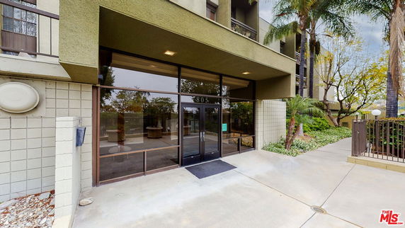 Front view of a modern multi-story building entrance with glass doors and a concrete walkway.