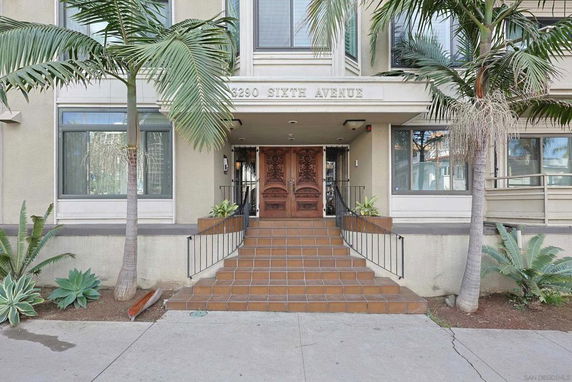 Front view of a multi-story building entrance with a staircase and wooden doors.