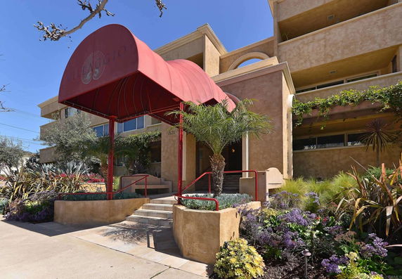 Front view of a multi-story building with a red awning and landscaped entrance.