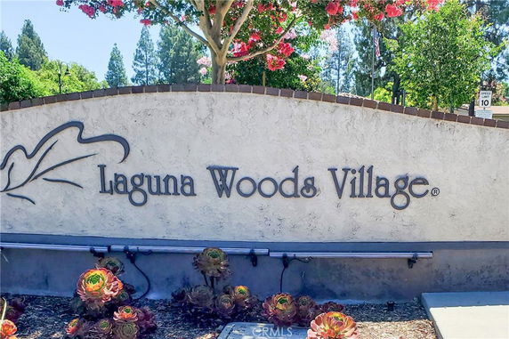 Wall with the inscription 'Laguna Woods Village' and plants in front.