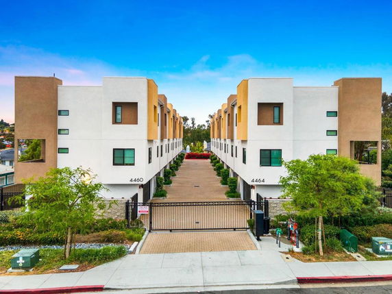 Front view of a modern multi-story apartment building with a gated entrance.