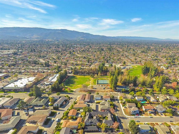 Aerial panoramic view of a suburban area with numerous houses, trees, and a visible tennis court and park in the middle ground.
