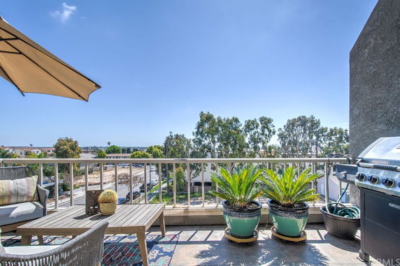 Balcony view with outdoor seating and a barbecue grill overlooking a suburban area with trees.