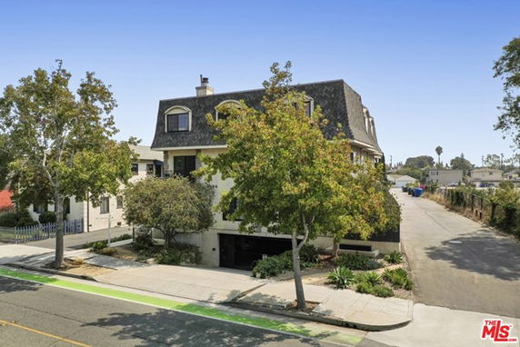 Front view of a multi-story house with a distinctive roof and plants around it.