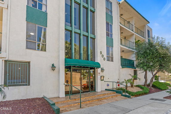 Front view of a multi-story building with a green awning over the entrance and balconies on upper levels.