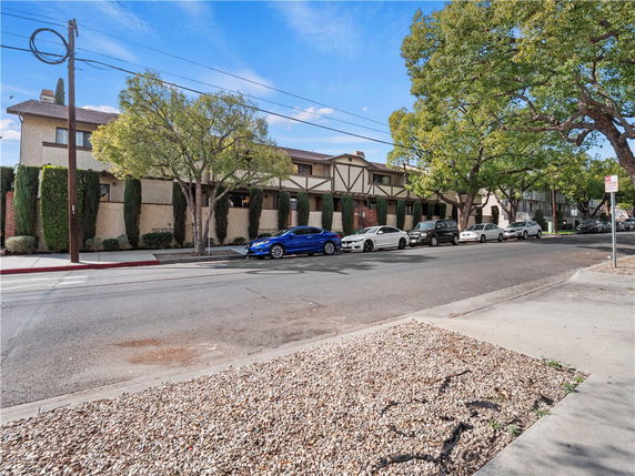 Front view of a two-story building with trees and parked cars along the street.
