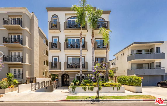 Front view of a multi-story residential building with balconies and palm trees.