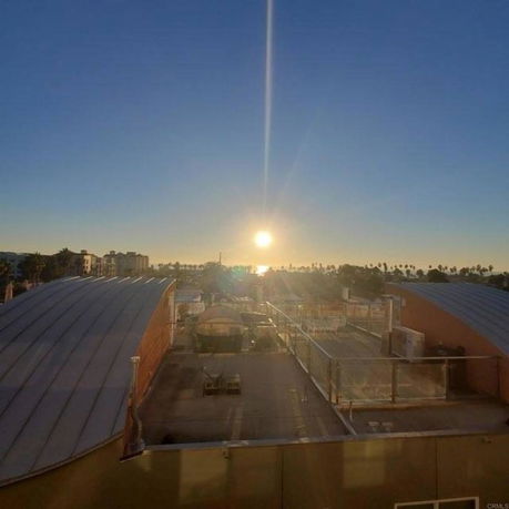 Rooftop view with curved structures, visible sunset, and distant palm trees.