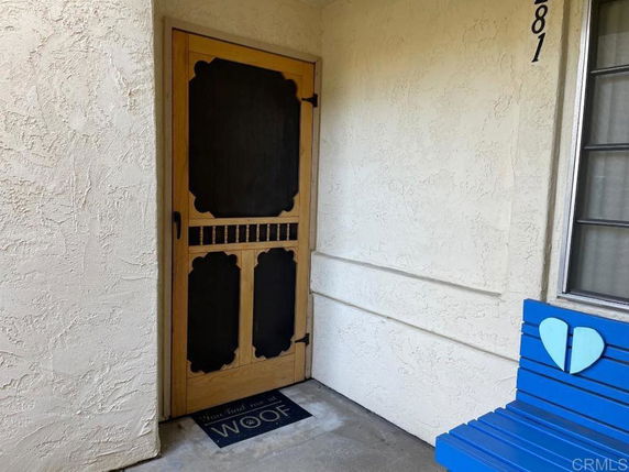 Entrance view with a wooden door and a blue bench beside it.