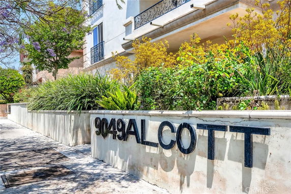 Front view of a residential building with a decorative wall sign reading 'ALCOTT' and surrounding greenery.