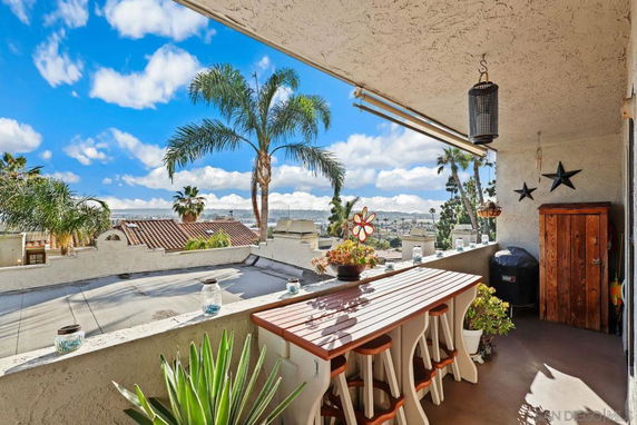 Outdoor balcony area with a table and chairs, overlooking a view with palm trees and rooftops.