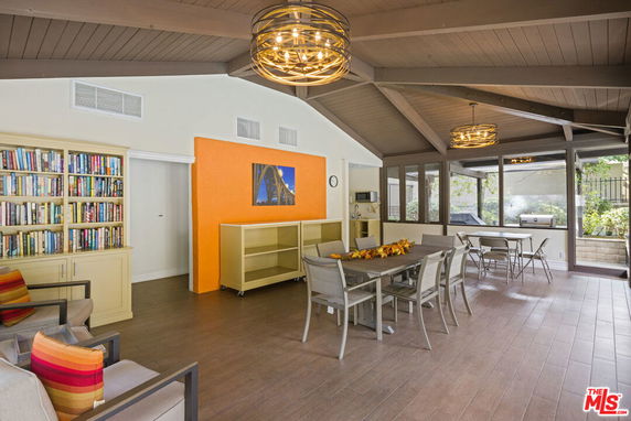 Indoor community room with tables, chairs, bookshelves, and large windows.