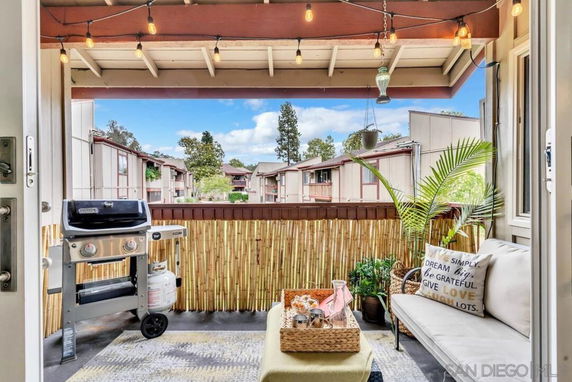 View from a balcony with outdoor seating and a grill, overlooking townhouses.