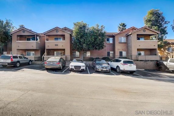 Front view of a two-story residential building with balconies and parked cars in front.
